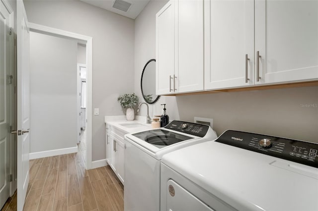 washroom with washing machine and dryer, sink, cabinets, and light wood-type flooring