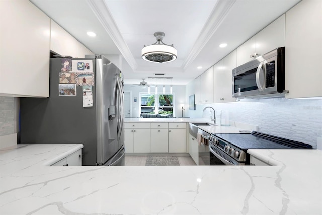 kitchen featuring white cabinets, decorative backsplash, a tray ceiling, light stone counters, and stainless steel appliances