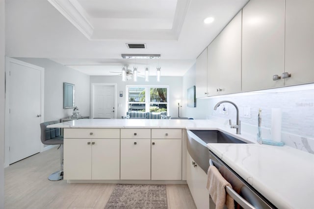 kitchen with sink, backsplash, kitchen peninsula, pendant lighting, and a tray ceiling