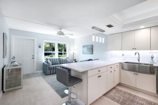 kitchen with kitchen peninsula, a breakfast bar, ceiling fan, sink, and decorative light fixtures