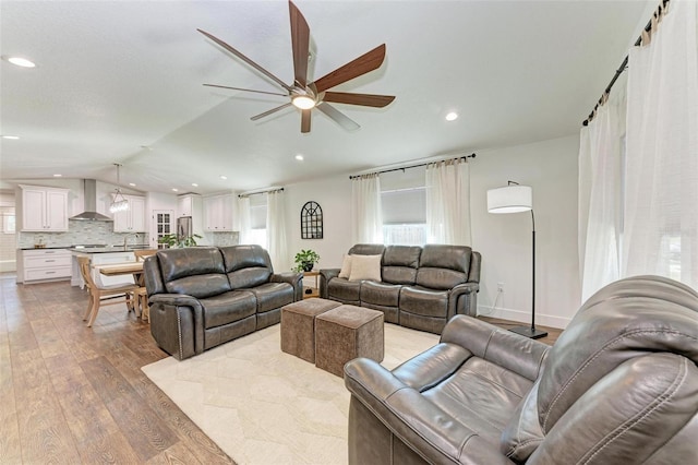 living room featuring light wood-type flooring, vaulted ceiling, ceiling fan, sink, and a barn door