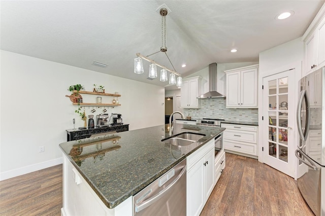 kitchen featuring white cabinets, wall chimney range hood, sink, an island with sink, and appliances with stainless steel finishes