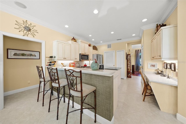 kitchen featuring stainless steel appliances, kitchen peninsula, crown molding, cream cabinetry, and a kitchen bar