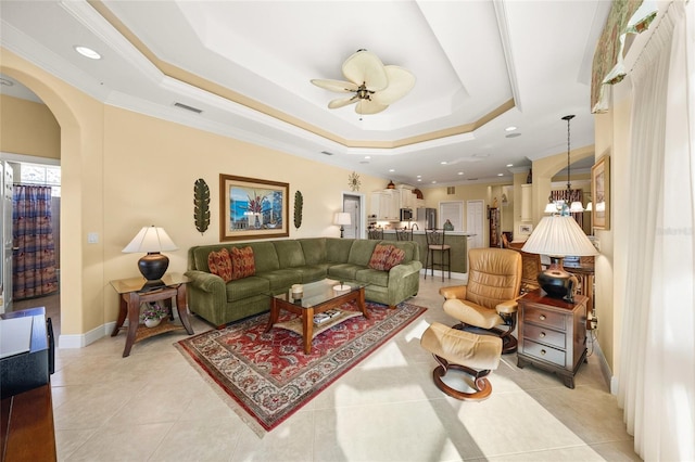 living room featuring light tile patterned floors, ceiling fan with notable chandelier, a raised ceiling, and crown molding