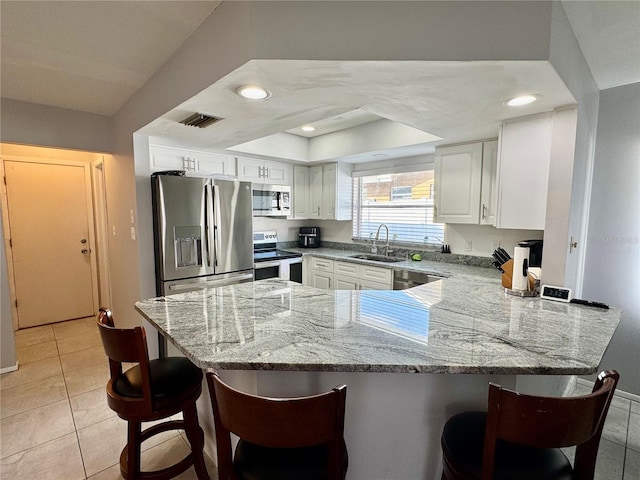 kitchen with white cabinetry, sink, light stone counters, kitchen peninsula, and appliances with stainless steel finishes