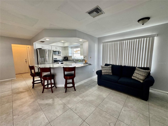 kitchen featuring kitchen peninsula, stainless steel appliances, sink, white cabinets, and a breakfast bar area