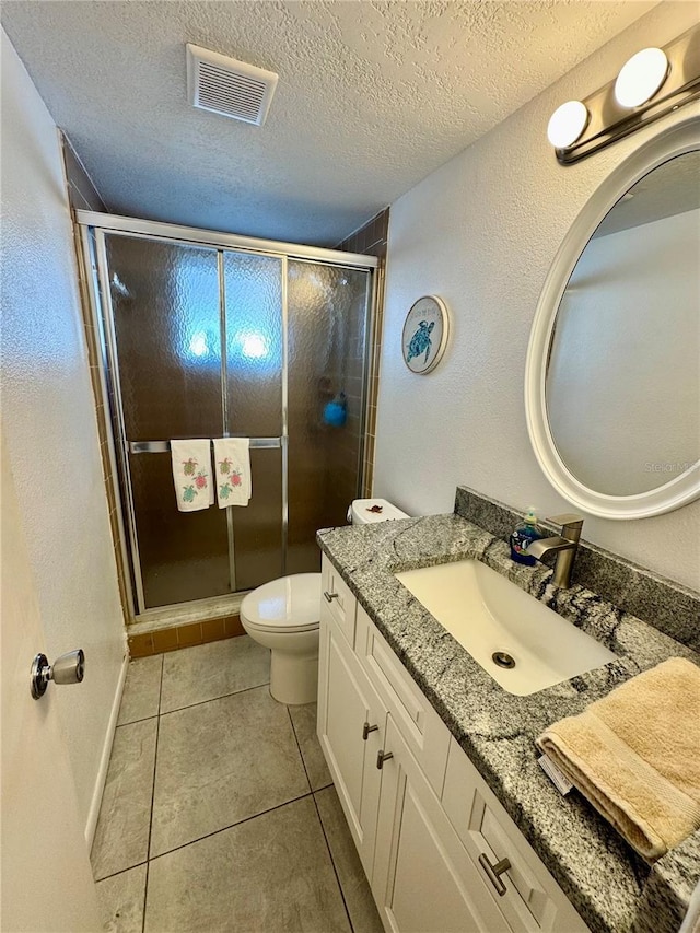 bathroom with vanity, a textured ceiling, a shower with door, tile patterned flooring, and toilet