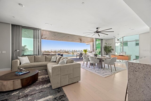 living room featuring a wall of windows, a water view, light hardwood / wood-style flooring, and ceiling fan