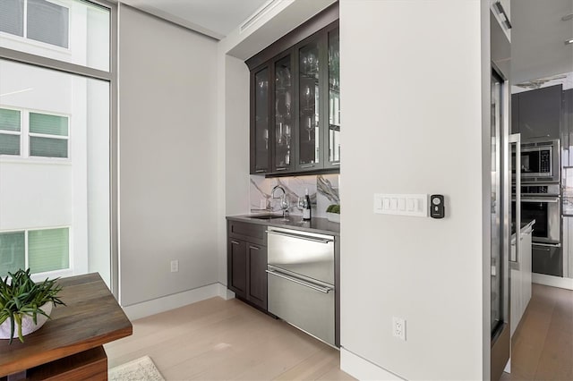 bar featuring sink, stainless steel appliances, light hardwood / wood-style flooring, decorative backsplash, and dark brown cabinets