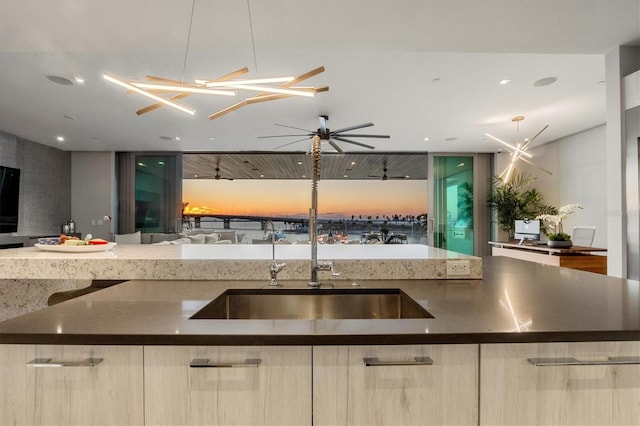 kitchen with ceiling fan, light brown cabinets, sink, dark stone countertops, and a center island with sink