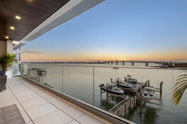 balcony at dusk featuring a water view and a dock