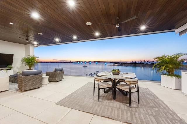 patio terrace at dusk with outdoor lounge area, a water view, and ceiling fan