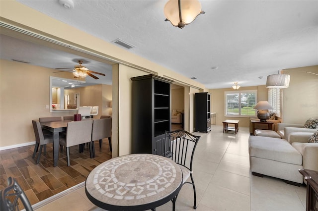 living room with a textured ceiling, light tile patterned floors, a ceiling fan, visible vents, and baseboards