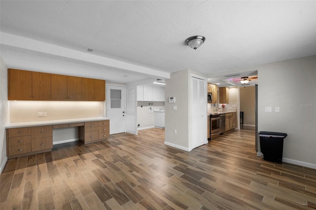 kitchen featuring built in study area, dark wood-style floors, brown cabinets, stainless steel appliances, and light countertops