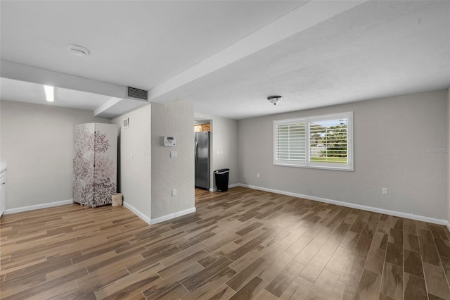 basement featuring freestanding refrigerator, visible vents, baseboards, and wood finished floors