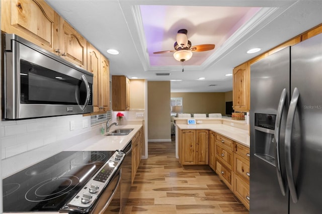 kitchen with a raised ceiling, a peninsula, stainless steel appliances, light countertops, and light wood-style floors