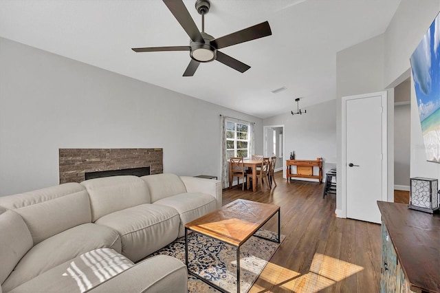 living room with ceiling fan with notable chandelier, dark hardwood / wood-style floors, a stone fireplace, and lofted ceiling