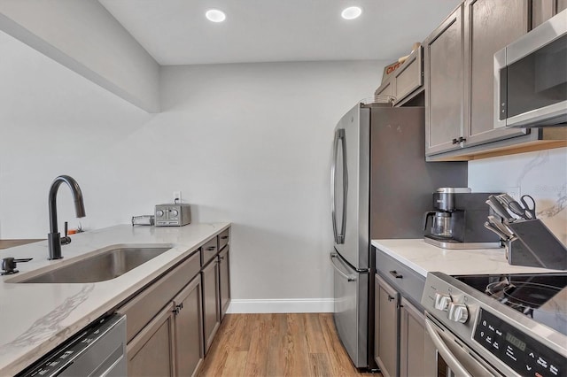 kitchen featuring sink, light stone countertops, stainless steel appliances, and light hardwood / wood-style flooring