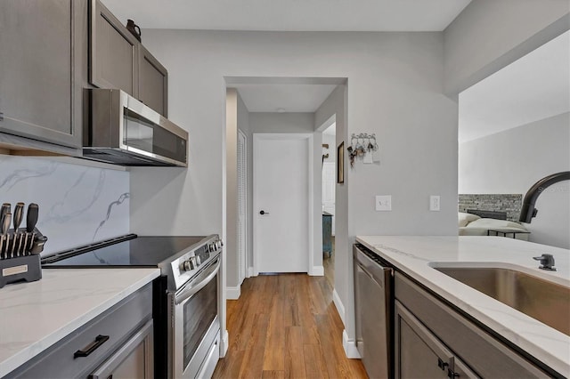 kitchen featuring sink, light stone countertops, tasteful backsplash, light hardwood / wood-style floors, and stainless steel appliances