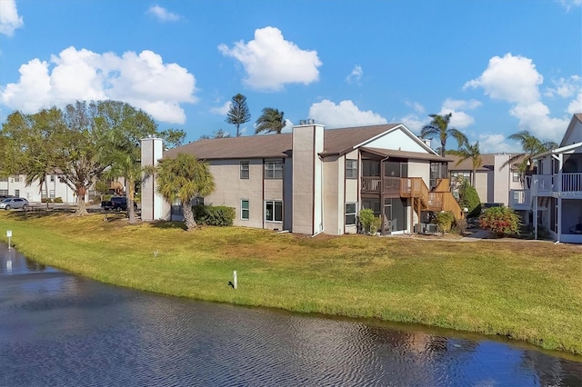 back of property with a yard, a balcony, and a water view