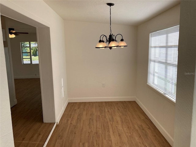 unfurnished dining area with ceiling fan with notable chandelier, a healthy amount of sunlight, and hardwood / wood-style flooring