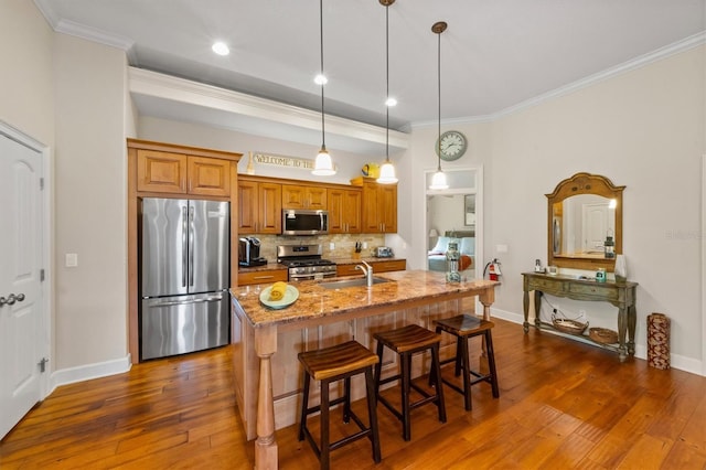 kitchen with light stone counters, pendant lighting, stainless steel appliances, an island with sink, and a breakfast bar area