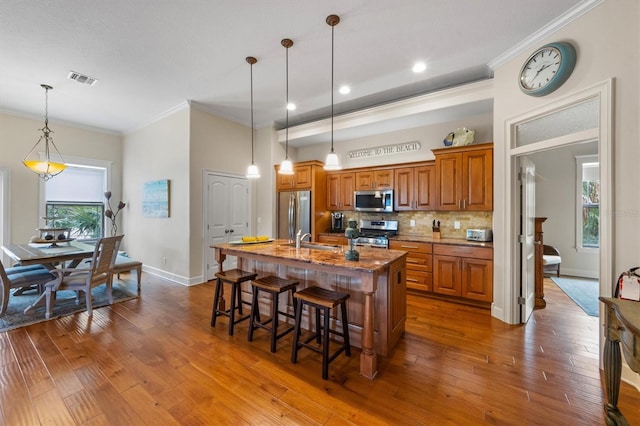 kitchen with decorative light fixtures, an island with sink, a breakfast bar, appliances with stainless steel finishes, and sink