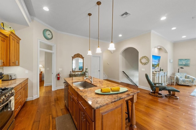 kitchen with light stone countertops, stainless steel appliances, an island with sink, crown molding, and sink