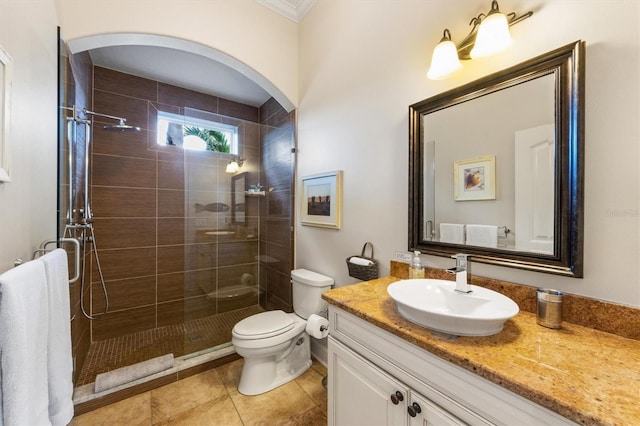 bathroom with toilet, tile patterned flooring, a tile shower, crown molding, and vanity