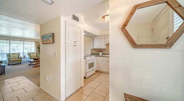 kitchen featuring electric stove, light colored carpet, tasteful backsplash, and white cabinets