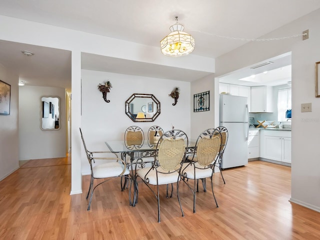 dining area featuring light wood-type flooring, sink, and an inviting chandelier