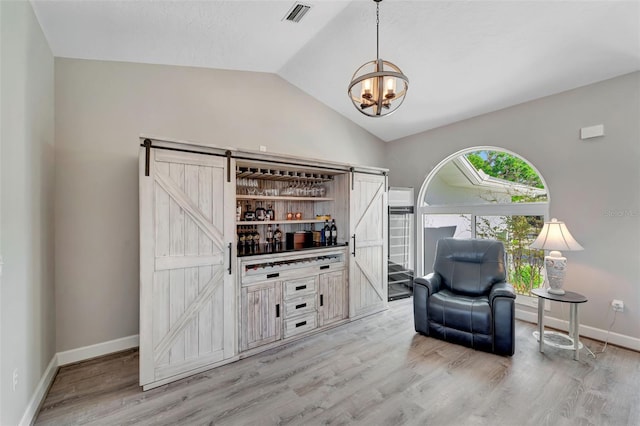 sitting room featuring a barn door, light hardwood / wood-style floors, an inviting chandelier, and lofted ceiling