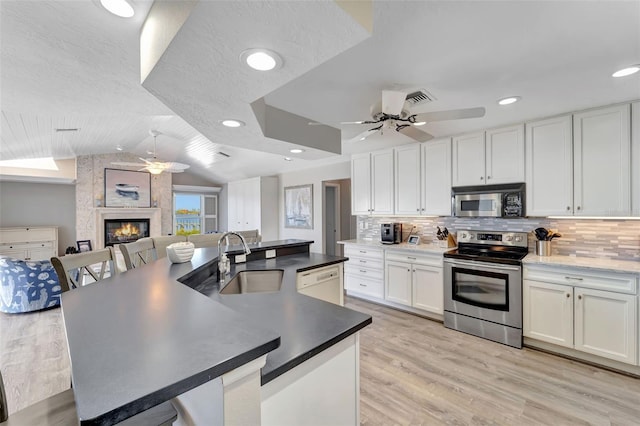 kitchen featuring a fireplace, white cabinetry, stainless steel range with electric cooktop, and sink