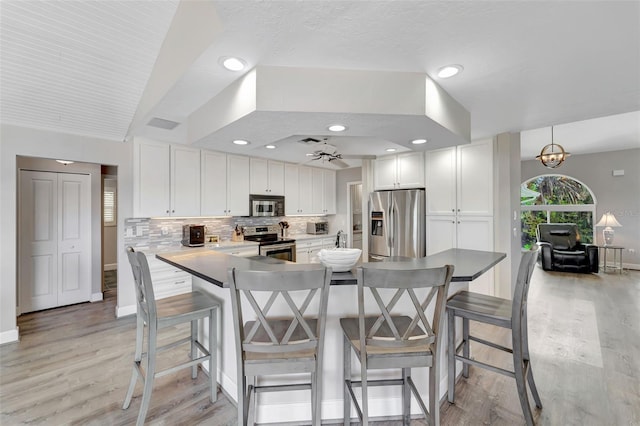 kitchen with a kitchen bar, white cabinets, stainless steel appliances, and decorative light fixtures