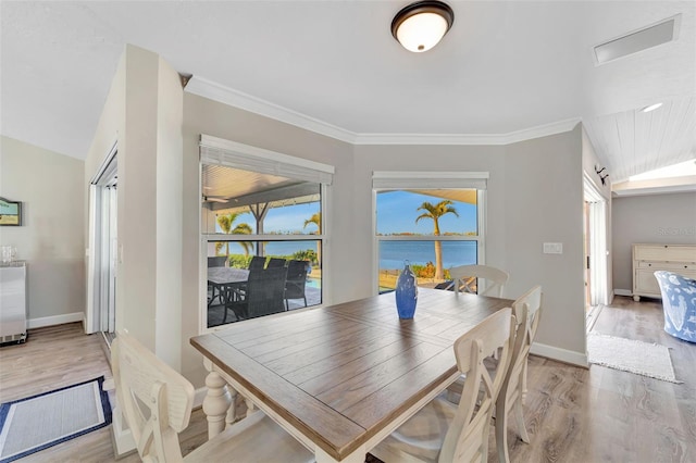 dining room featuring crown molding, a water view, vaulted ceiling, and hardwood / wood-style flooring