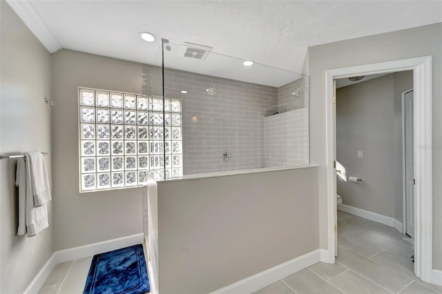 bathroom featuring tiled shower, tile patterned flooring, and toilet