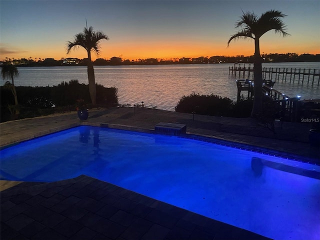 pool at dusk featuring a boat dock and a water view