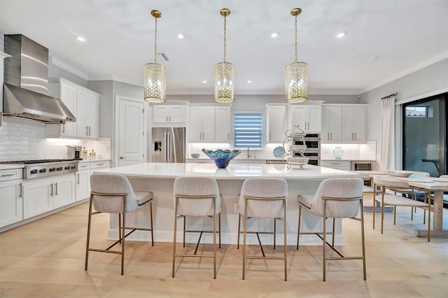 kitchen with wall chimney range hood, a spacious island, stainless steel appliances, and decorative light fixtures