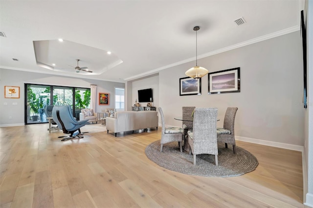 dining area with ceiling fan, light wood-type flooring, ornamental molding, and a tray ceiling