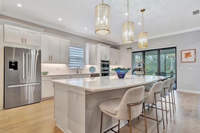 kitchen featuring appliances with stainless steel finishes, a kitchen island, decorative light fixtures, light hardwood / wood-style flooring, and white cabinetry