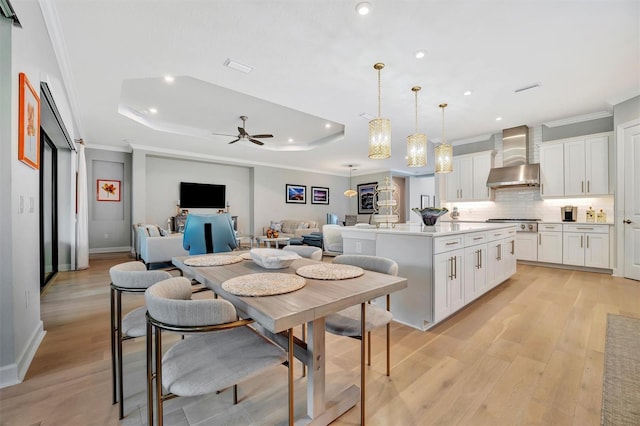 kitchen featuring white cabinetry, a center island, wall chimney exhaust hood, decorative light fixtures, and a tray ceiling