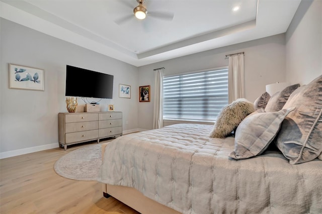 bedroom featuring light wood-type flooring, a raised ceiling, and ceiling fan