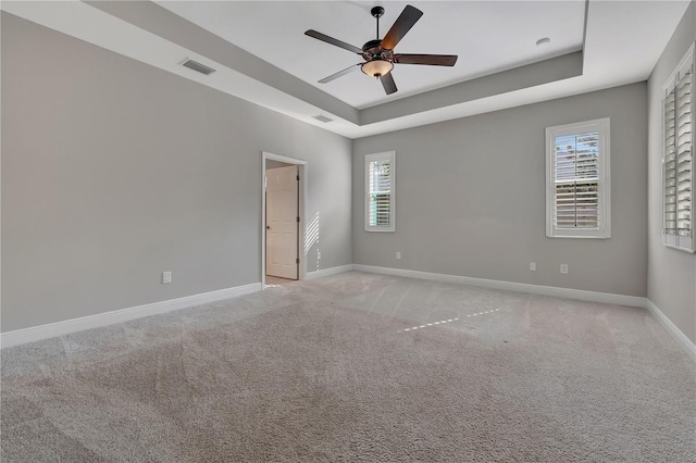 empty room featuring ceiling fan, light colored carpet, plenty of natural light, and a tray ceiling