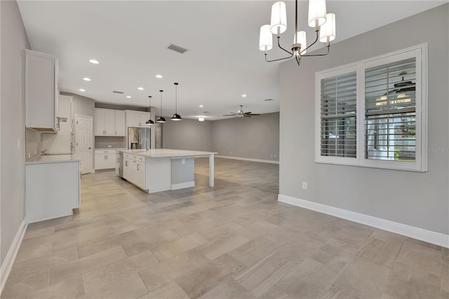 kitchen featuring ceiling fan with notable chandelier, decorative light fixtures, white cabinetry, an island with sink, and stainless steel fridge