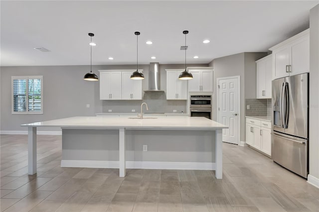 kitchen with white cabinetry, an island with sink, appliances with stainless steel finishes, hanging light fixtures, and wall chimney exhaust hood