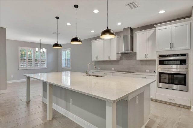 kitchen featuring pendant lighting, wall chimney exhaust hood, a spacious island, and sink