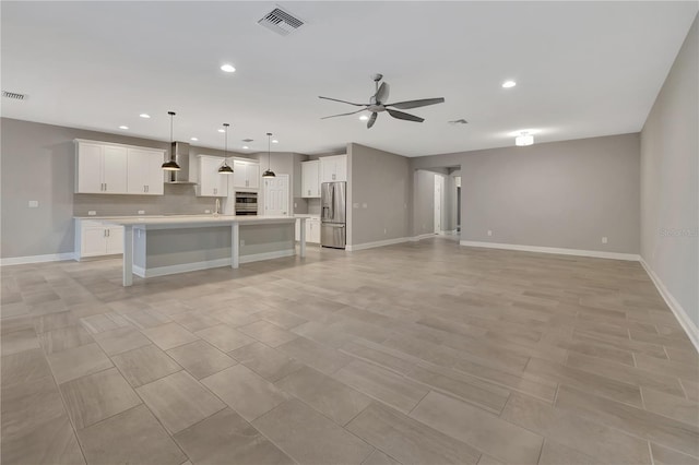 kitchen featuring an island with sink, stainless steel appliances, decorative light fixtures, wall chimney exhaust hood, and white cabinets