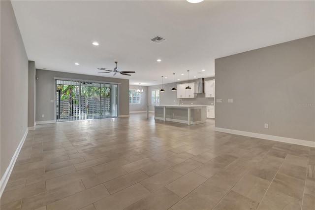 unfurnished living room with ceiling fan with notable chandelier and sink