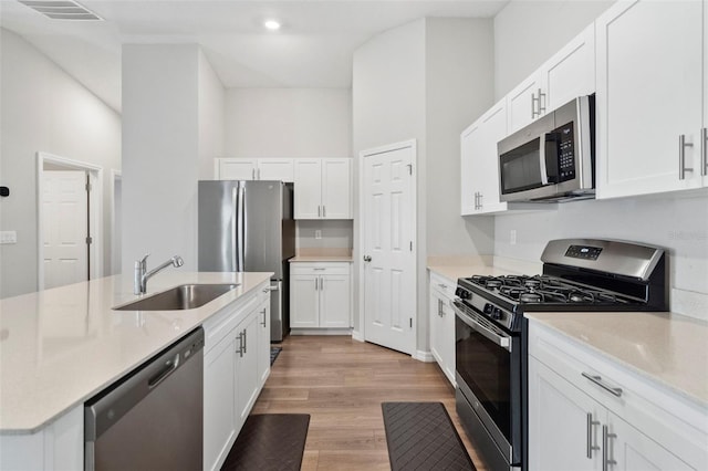 kitchen featuring stainless steel appliances, sink, a high ceiling, light hardwood / wood-style floors, and white cabinetry