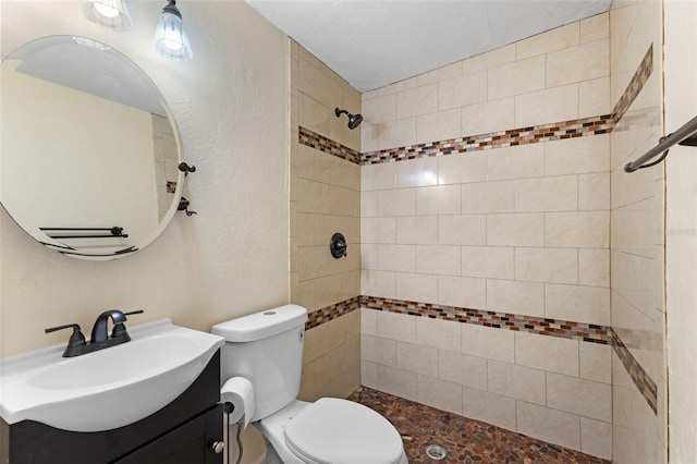 bathroom with tiled shower, vanity, and toilet